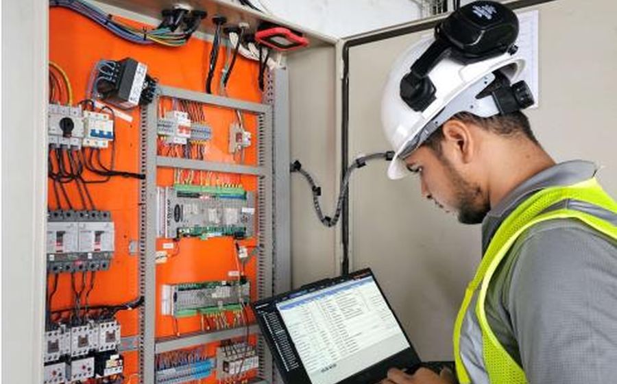Technicien mettant en service une armoire de contrôle avec un ordinateur portable sur le chantier